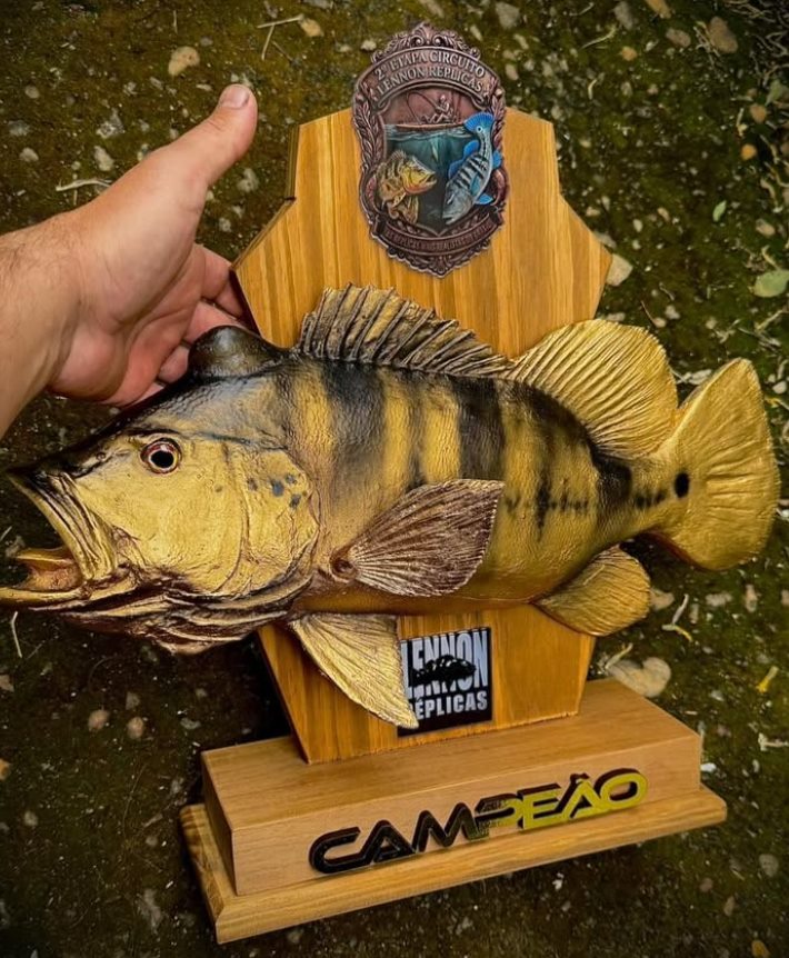 Troféu de campeonato: réplica de tucunaré na base de madeira com o brasão da etapa e a base gravada CAMPEÃO